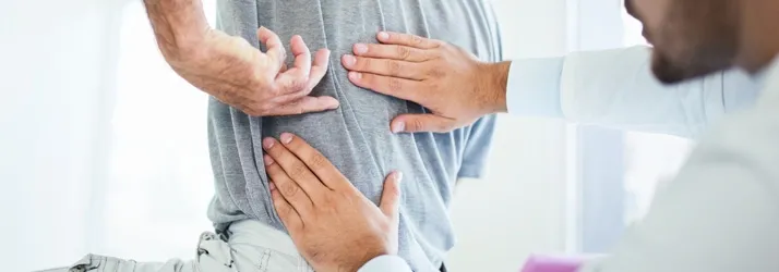 Close-up of hands placed on a person’s lower back while another person examines the lumbar area.