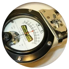 Close-up of a handheld analog measuring instrument with a circular dial, pointer, and metallic housing.